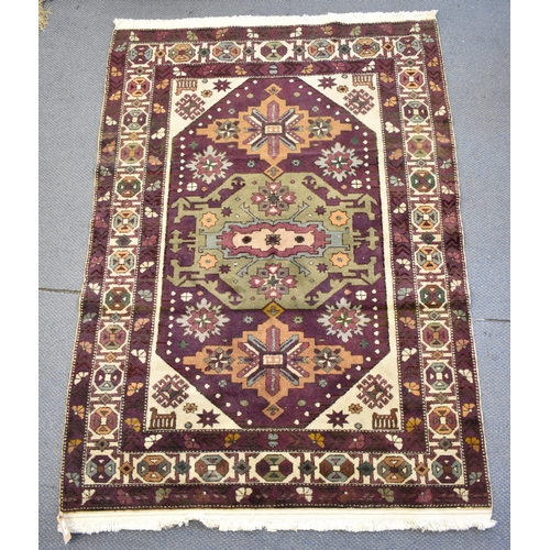 247 - A Kazak rug with three medallions on a purple ground, in green, blue and brown with off white spandr... 