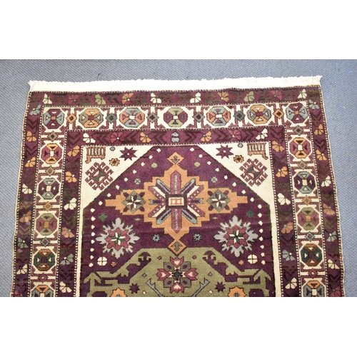 247 - A Kazak rug with three medallions on a purple ground, in green, blue and brown with off white spandr... 