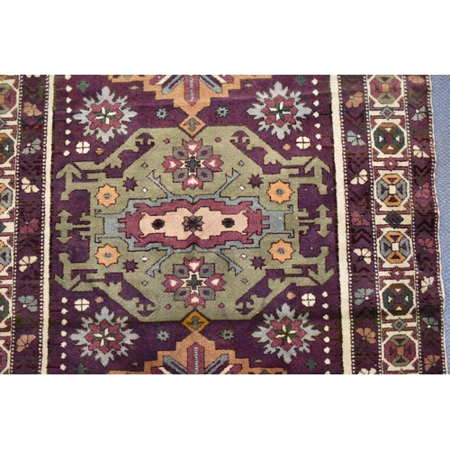 247 - A Kazak rug with three medallions on a purple ground, in green, blue and brown with off white spandr... 