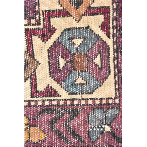 247 - A Kazak rug with three medallions on a purple ground, in green, blue and brown with off white spandr... 