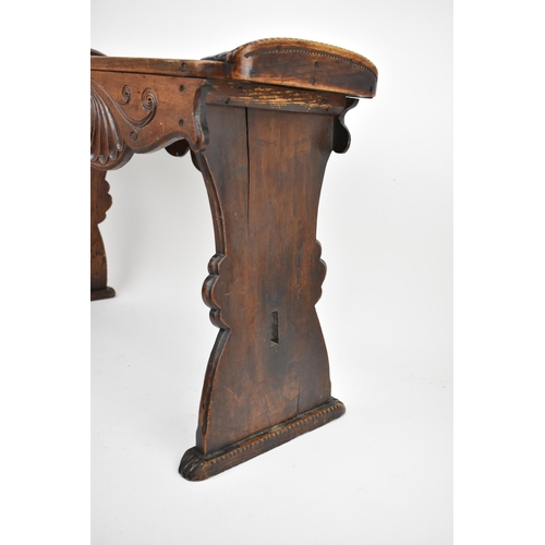 233 - A 19th century continental oak stool, the carved top with upturned ends and a shaped apron, on splay... 