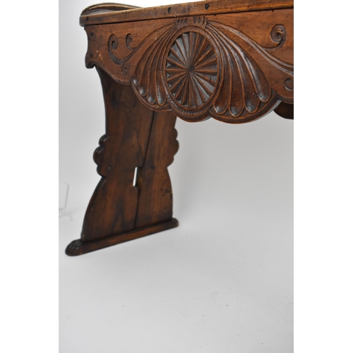 233 - A 19th century continental oak stool, the carved top with upturned ends and a shaped apron, on splay... 