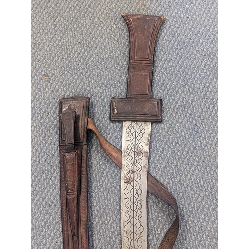 304 - An African tribal sword having a 77cm curved blade engraved to both sides together with leather scab... 