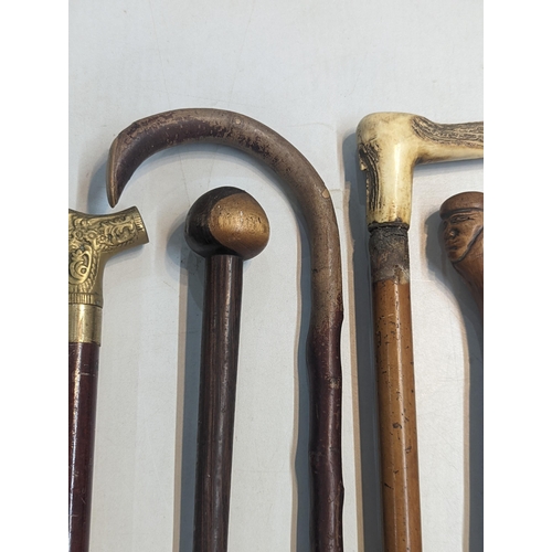 454 - A group of six walking sticks having mixed carved wood and bone handles and one brass example, anoth... 