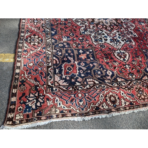 490 - An Iranian hand woven carpet having a red ground, geometric motifs and tasselled ends, 372cm x 300cm... 