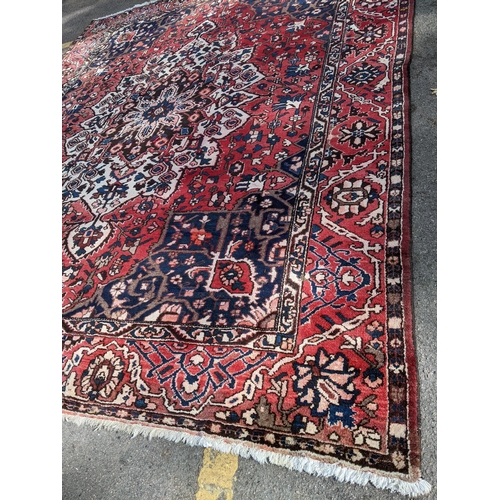 490 - An Iranian hand woven carpet having a red ground, geometric motifs and tasselled ends, 372cm x 300cm... 