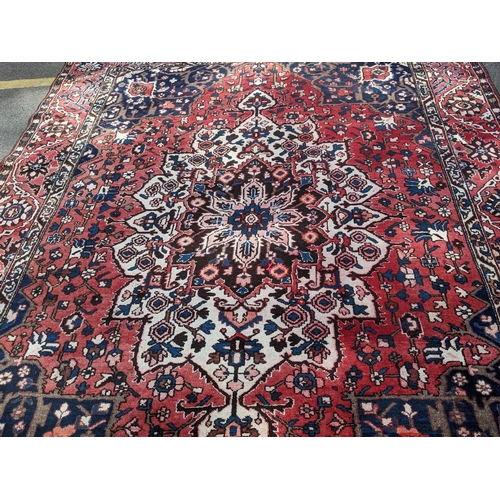 490 - An Iranian hand woven carpet having a red ground, geometric motifs and tasselled ends, 372cm x 300cm... 