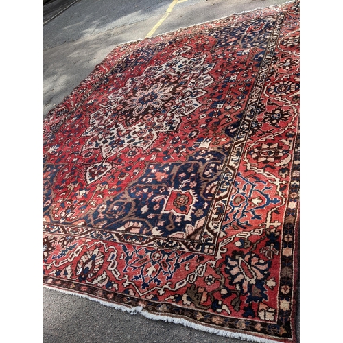 490 - An Iranian hand woven carpet having a red ground, geometric motifs and tasselled ends, 372cm x 300cm... 