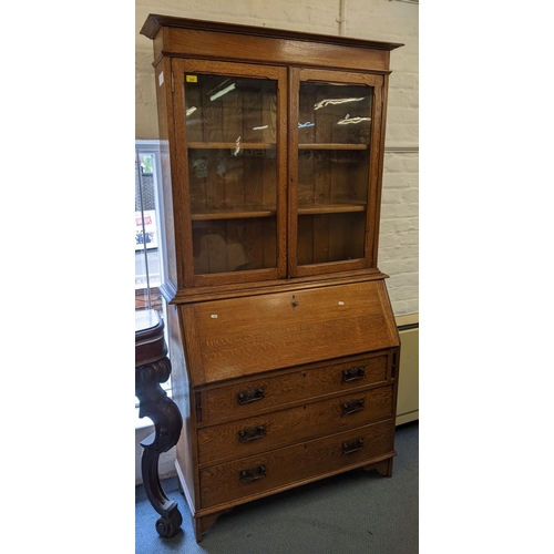 445 - An Arts & Crafts oak bureau bookcase having twin glazed doors above a fall flap and three drawers, 2... 