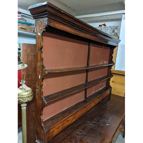 495 - A Georgian fruitwood dresser having a plate rack above three drawers, shaped apron and on turned tap... 