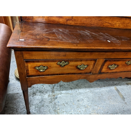 495 - A Georgian fruitwood dresser having a plate rack above three drawers, shaped apron and on turned tap... 