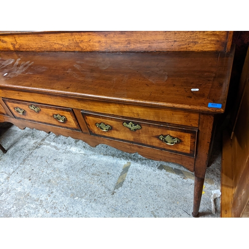 495 - A Georgian fruitwood dresser having a plate rack above three drawers, shaped apron and on turned tap... 