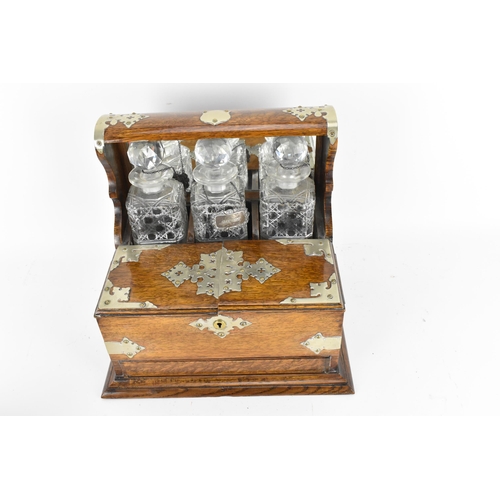 296 - A Victorian white metal mounted oak tantalus, containing three cut glass decanters, with hallmarked ... 