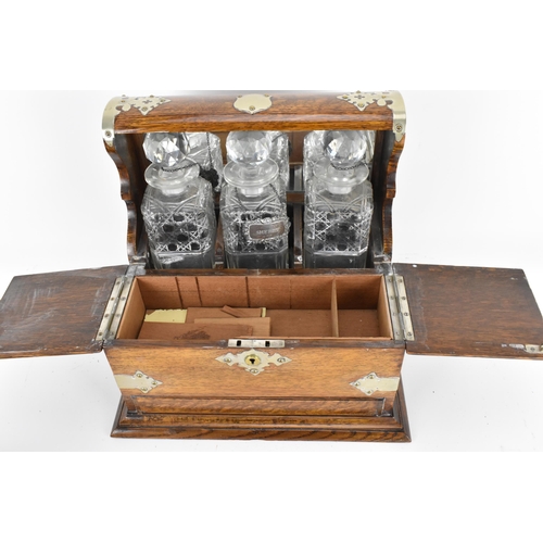 296 - A Victorian white metal mounted oak tantalus, containing three cut glass decanters, with hallmarked ... 