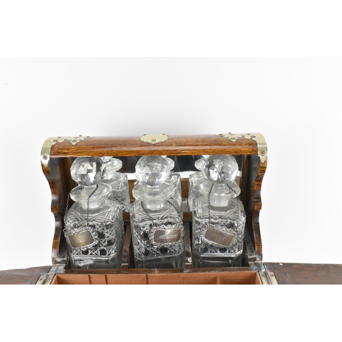 296 - A Victorian white metal mounted oak tantalus, containing three cut glass decanters, with hallmarked ... 