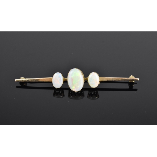 148 - A yellow metal and opal brooch, with three central oval cabochon opals on a plain bar setting, 7 cm ... 