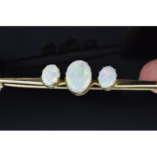 148 - A yellow metal and opal brooch, with three central oval cabochon opals on a plain bar setting, 7 cm ... 