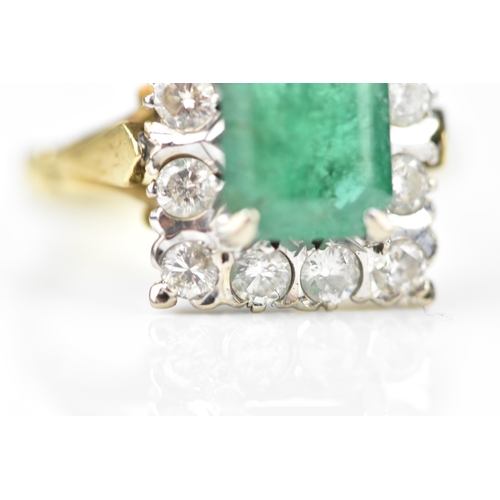 153 - An 18ct yellow gold, emerald and diamond dress ring, with central step cut emerald in a halo of twel... 