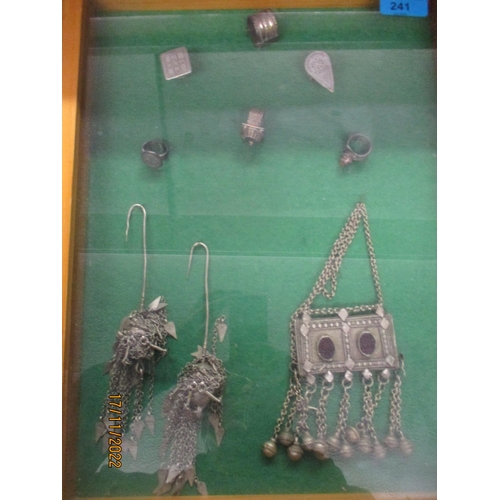 241 - A framed and glazed and mounted group of Middle Eastern white metal jewellery, some set with coloure... 