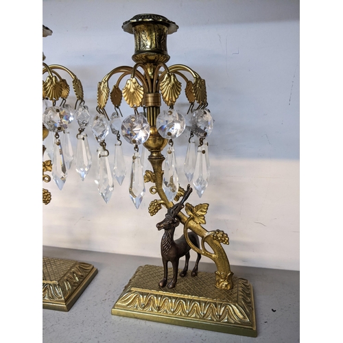 233 - A pair of mid 20th century gilt metal crystal drop candlesticks in the form of stags standing under ... 