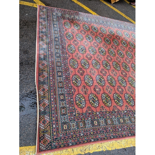 606 - A Middle Eastern machine woven red ground rug having repeating motifs and multiguard borders, 347cm ... 