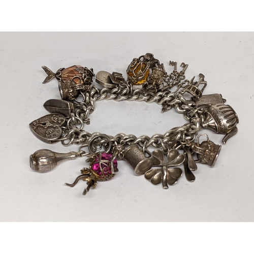 115 - A silver charm bracelet with mixed charms to include a heart shaped locket, four leaf clover, teapot... 