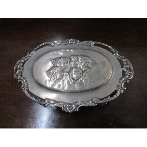 156 - An Edwardian VII silver oval dressing table box, repoussé decorated with winged heads to the lid sur... 