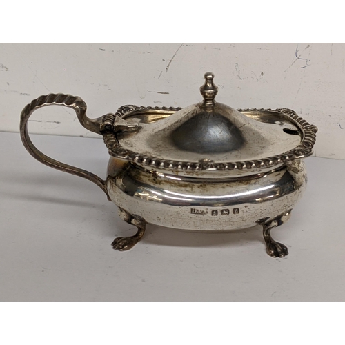 94 - An early 20th century silver mustard pot having gadrooned rim and lion paw feet, 85.7g excluding lin... 