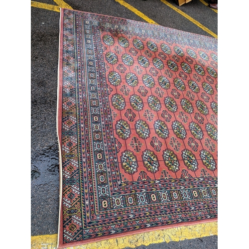 440 - A Middle Eastern machine woven red ground rug having repeating motifs and multiguard borders, 347cm ... 