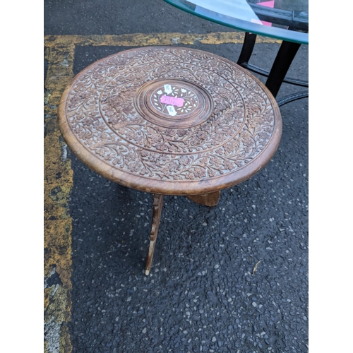 194 - A modern cast metal coffee table with a glass top, together with a teak Indian carved occasional tab... 