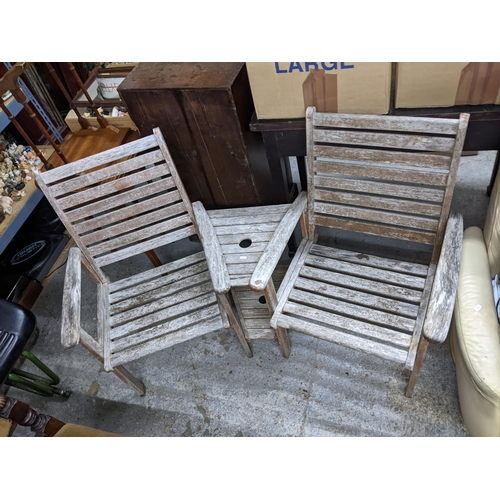 251 - A weathered teak slatted garden bench of two seats with central table of triangular form with space ... 