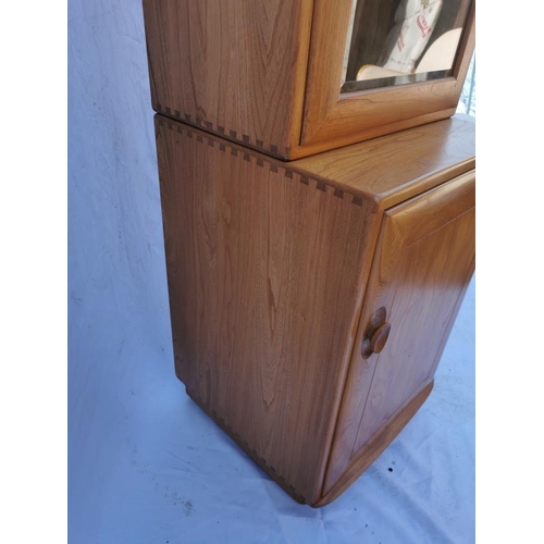 394 - A light elm Ercol glazed tall cabinet, with single glazed door above a cupboard enclosing a single s... 