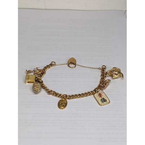 27 - A 9ct gold charm bracelet with charms, to include an 18ct gold charm, a 9ct charm in the form of a t... 