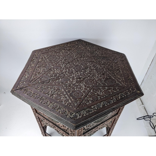 77 - An early 20th century Indian carved hardwood table with hexagonal top on a folding base, 66cm high, ... 