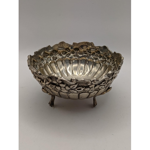 103 - A three footed embossed, continental silver dish, together with a white metal whiskey label, total w... 