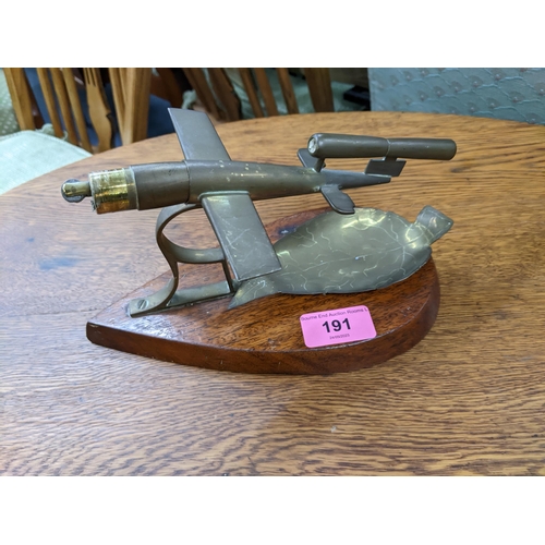 191 - A brass desk lighter modelled as a V-1 rocket, mounted on a tear shaped mahogany base with brass lea... 