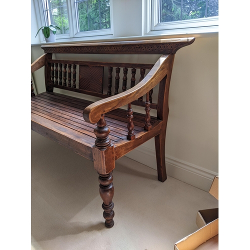 289 - A Thai stained softwood bench with a carved and spindle back and slatted seat on turned legs, 128cm ... 