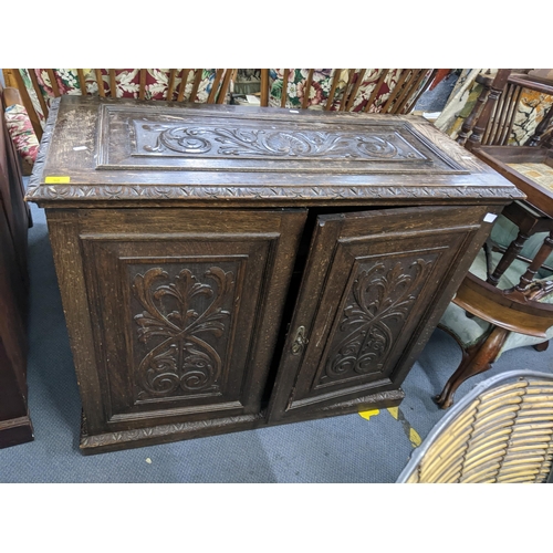 90 - A late 19th/early 20th century oak cabinet having carved panelled top and doors, loose shelves and o... 