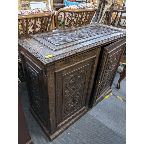 90 - A late 19th/early 20th century oak cabinet having carved panelled top and doors, loose shelves and o... 