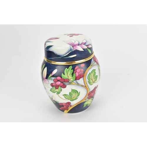 77 - A Moorcroft enamels miniature lidded vase, designed with florals and foliage on a white and dark blu... 