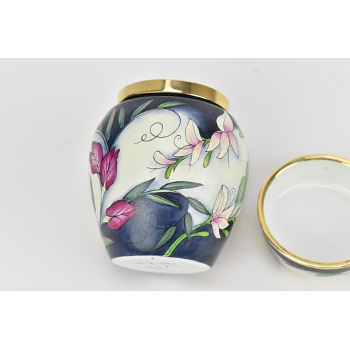 77 - A Moorcroft enamels miniature lidded vase, designed with florals and foliage on a white and dark blu... 