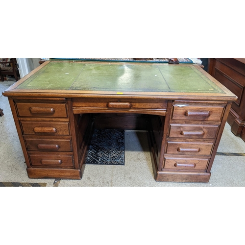 511 - A 1940's twin pedestal writing desk having a green leather topped scriber, nine drawers and on a pli... 