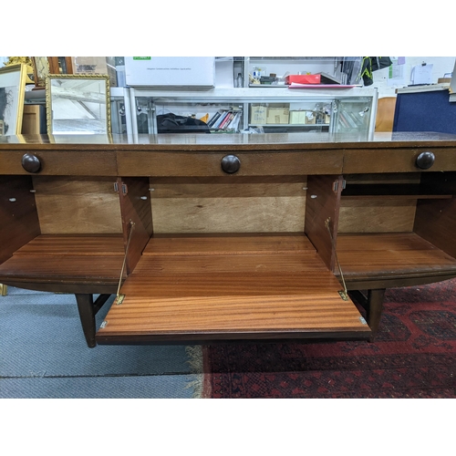 85 - An Elliots of Newbury bow fronted teak sideboard with three drawers over three cupboards on tapered ... 