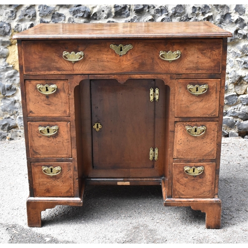 135 - An early George III walnut and feather-banded kneehole desk, the bookmatched veneer top with herring... 