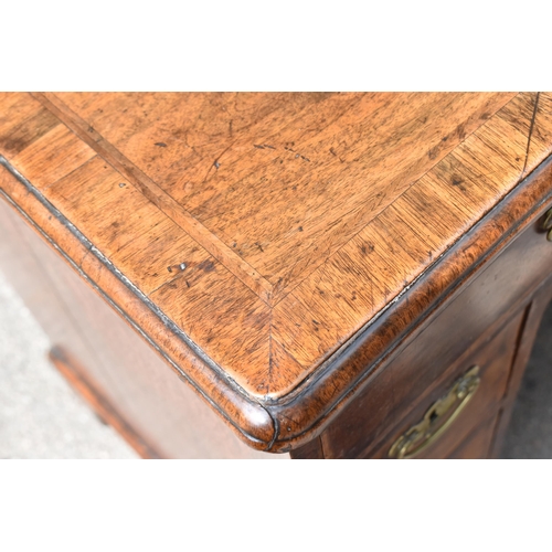 135 - An early George III walnut and feather-banded kneehole desk, the bookmatched veneer top with herring... 