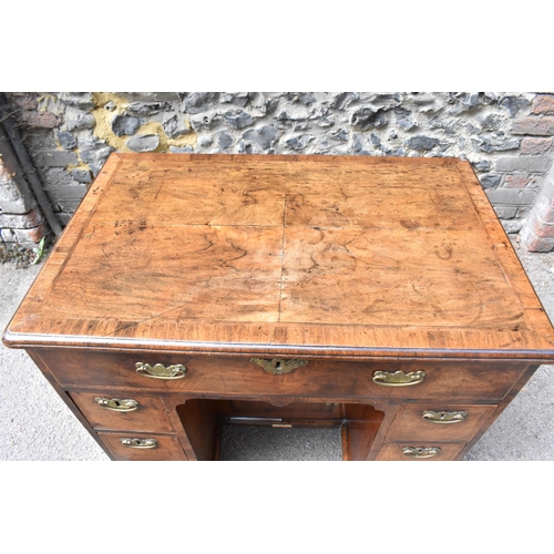 135 - An early George III walnut and feather-banded kneehole desk, the bookmatched veneer top with herring... 