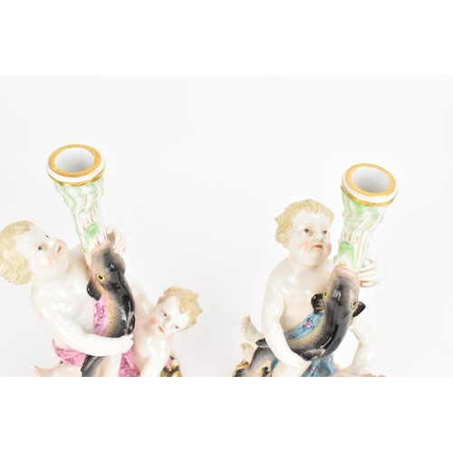 152 - Two Meissen figural candlesticks, 19th century, each modelled as two putti supporting a fish issuing... 