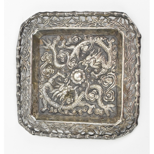 69 - A Chinese export white metal pin dish, circa 1900, of square form with embossed dragons chasing the ... 