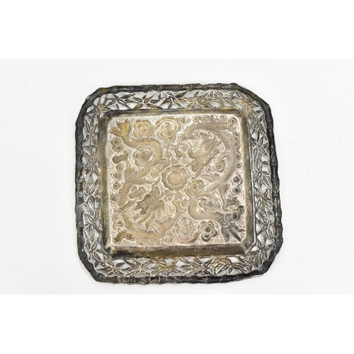 69 - A Chinese export white metal pin dish, circa 1900, of square form with embossed dragons chasing the ... 