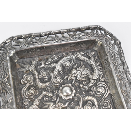 69 - A Chinese export white metal pin dish, circa 1900, of square form with embossed dragons chasing the ... 